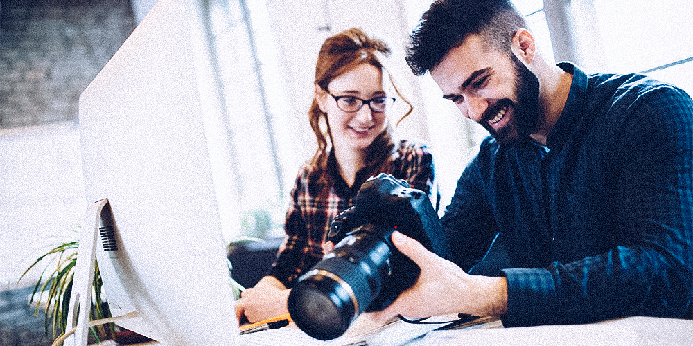 Mann und Frau mit Kamera vorm Mac zur Bildbearbeitung